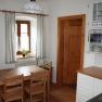 Kitchen, © Grünfelder Small kitchen with wooden furniture, dining table, chairs and a window with curtains.