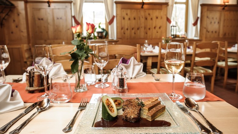 Set table, © Roman Siebenhandl An elegantly laid table in a rustic restaurant with a plate of gourmet food, wine glasses and a vase of roses.