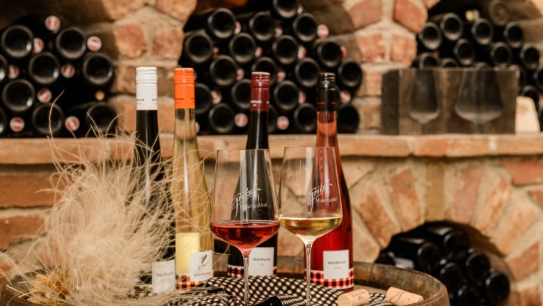 Gritsch, © Best of Wachau/Rita Newmann Wine bottles and glasses in front of a shelf with wine bottles in a wine cellar.