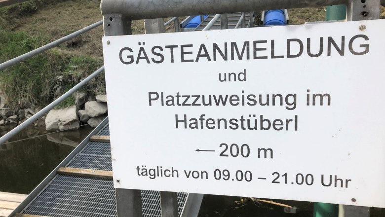 Anmeldung Sportboothafen, © Donau NÖ Tourismus GmbH Ein Schild mit der Aufschrift 'Gästeanmeldung und Platzzuweisung im Hafenstüberl, 200 m, täglich von 09.00 – 21.00 Uhr'.