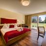 Genießerzimmer in der Gartenvilla, © Photography Pfeffel Gemütliches Hotelzimmer mit Doppelbett, roten Akzenten und Blick auf den Garten durch große Fenster.