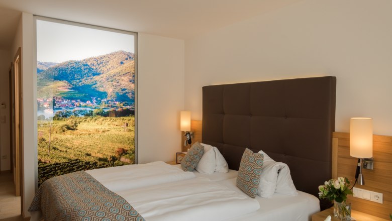 Donauhof double room, © Marcella Wallner Modern hotel room with double bed, decorative cushions and large landscape picture on the wall.