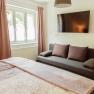 Appartement 2, © Ines Nejedly Innenansicht eines Schlafzimmers mit Bett, Sofa, Fenster und Wandfernseher.
