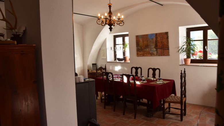 Revealed in the Ross stable, © Georg Smolka A dining room with a table set with a red tablecloth. A painting hangs on the wall and a chandelier hangs from the ceiling.