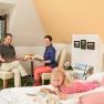 Room, © Hamberger Family in a cozy room, parents reading at the table, child lying on the bed with a book.