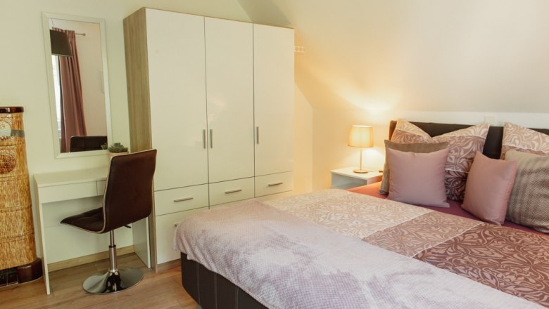 Appartement 2, © Ines Nejedly Schlafzimmer mit Doppelbett, Kleiderschrank, Schminktisch und Lampe.