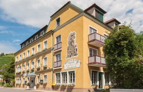 Stierschneider's Weinhotel Wachau, © Johann Perger Yellow hotel building with balconies and plants, blue sky in the background.