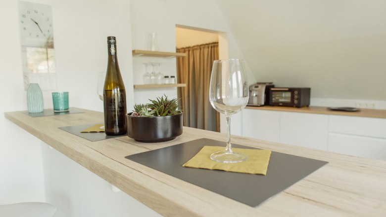 Appartement 2, © Ines Nejedly Moderne Küche mit Bartresen, Weinglas und Flasche.