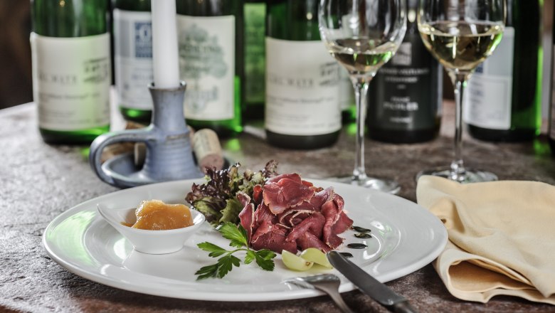 Speisenbeispiel vom Hotel Restaurant Zum Schwarzen Bären, © BOW Rita Newman Ein Teller mit Schinken, Salat und Chutney, umgeben von Weinflaschen und Gläsern auf einem Tisch.