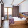 Zimmer mit Balkon, © Martina Siebenhandl Ein gemütliches Hotelzimmer mit Holzmöbeln, einem Doppelbett, Balkon und dekorativen Kissen.