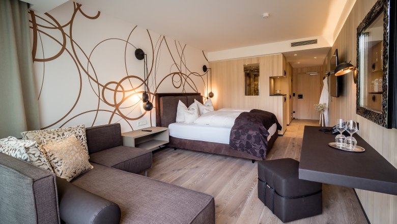 Zimmerbeispiel, © Alexander Pfeffel Photography Modern eingerichtetes Hotelzimmer mit Doppelbett, Sofa und Schreibtisch.