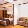 Zimmeransicht, © Martina Siebenhandl Gemütliches Hotelzimmer mit Holzmöbeln, Doppelbett, Sofa und kleinem Tisch.