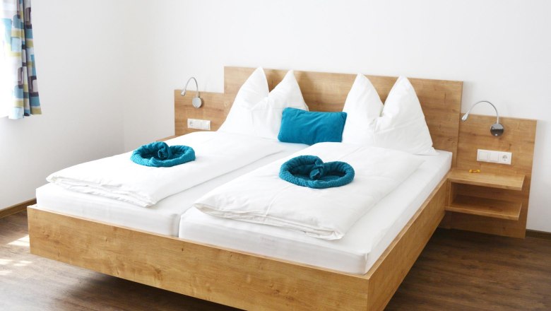 Guest room, © Familie Martin Modern guest room with double bed, white comforters and blue pillows.