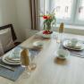 Apartment 1, © Ines Nejedly A dining table set with crockery, glasses and flowers in a bright room.
