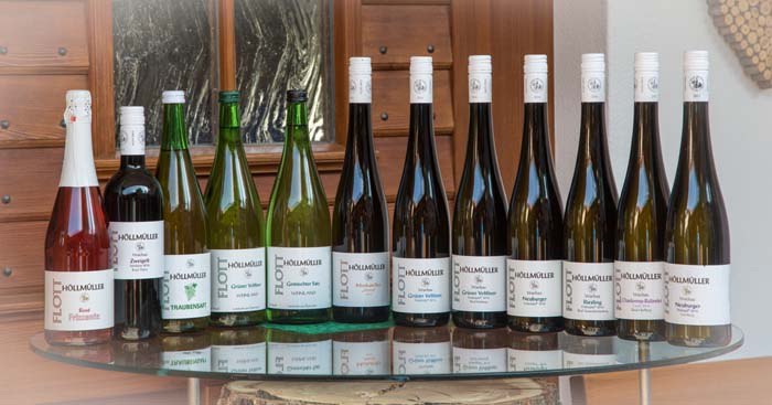 12b1165, © Josef Salomon Eine Auswahl von Weinflaschen auf einem Glastisch vor einer Holzwand.