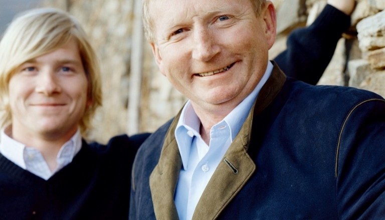 Hirtzberger Franz, © Jellasitz Zwei Männer stehen vor einer Steinmauer, einer lächelt in die Kamera.