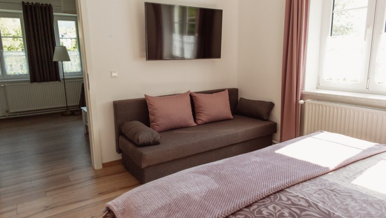 Appartement 1, © Ines Nejedly Modernes Wohnzimmer mit Sofa, Flachbildfernseher und Fenster mit rosa Vorhängen.