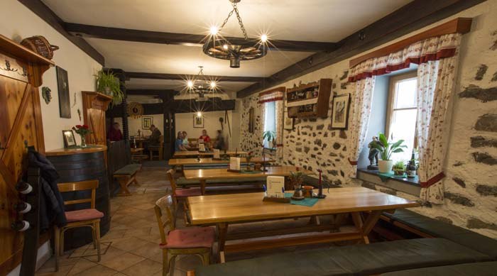 12b4566, © Josef Salomon Gemütlicher Gastraum mit Holztischen und Steinwänden.