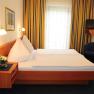 Haus Oestreicher, © Haus Oestreicher Ein Hotelzimmer mit Doppelbett, blauen Vorhängen und einem kleinen Fernseher an der Wand.