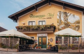 Wanderhof mit Aussichtsplattform, © Niederösterreich Werbung/Daniela Führer Ein traditionelles Gasthaus mit Balkon und Wandgemälde, umgeben von Sonnenschirmen und Pflanzen.