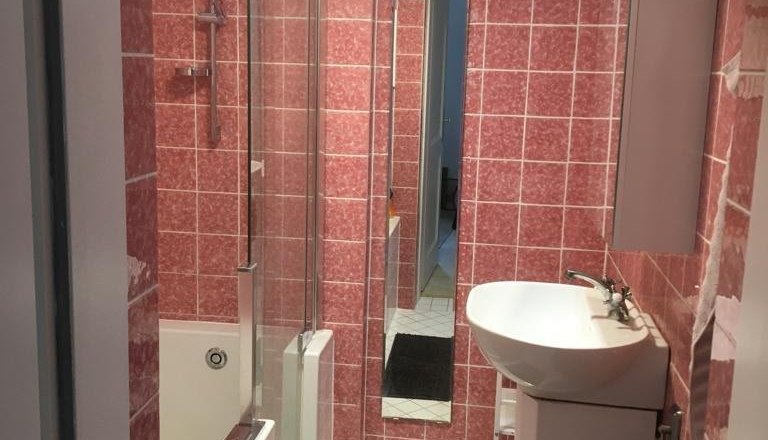 Kleines Badezimmer mit rosa Fliesen, Badewanne, Waschbecken und Spiegel.