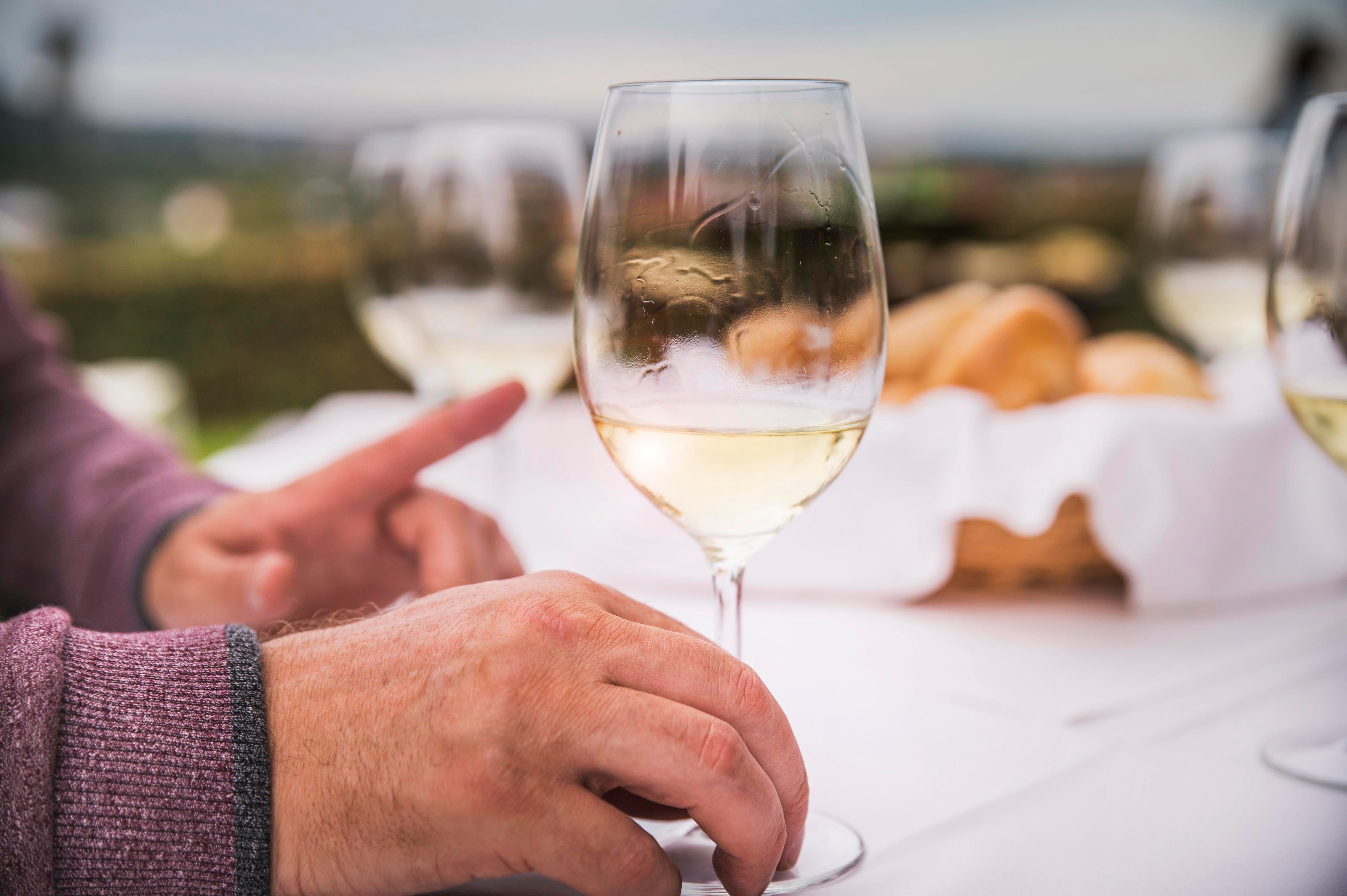 Nahaufnahme von Händen mit Weinglas auf gedecktem Tisch im Freien.