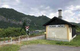 Small station building in Willendorf in the Wachau, surrounded by green hills and railroad tracks.