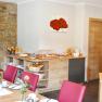 A breakfast buffet in a cozy room with red chairs, wooden furniture and a stone wall. The buffet includes croissants, muesli and orange juice.