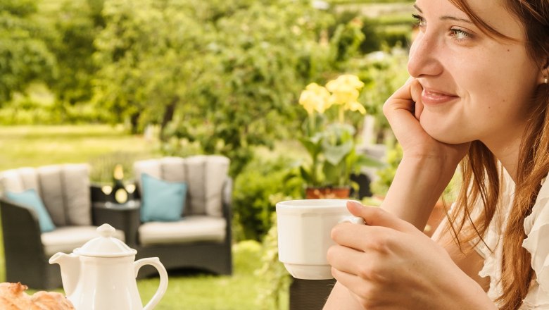 Frau genießt Kaffee im Freien mit Blick auf Weinberge.