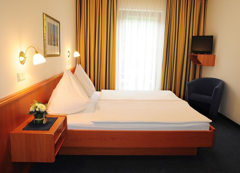 Ein Hotelzimmer mit Doppelbett, blauen Vorhängen und einem kleinen Fernseher an der Wand.