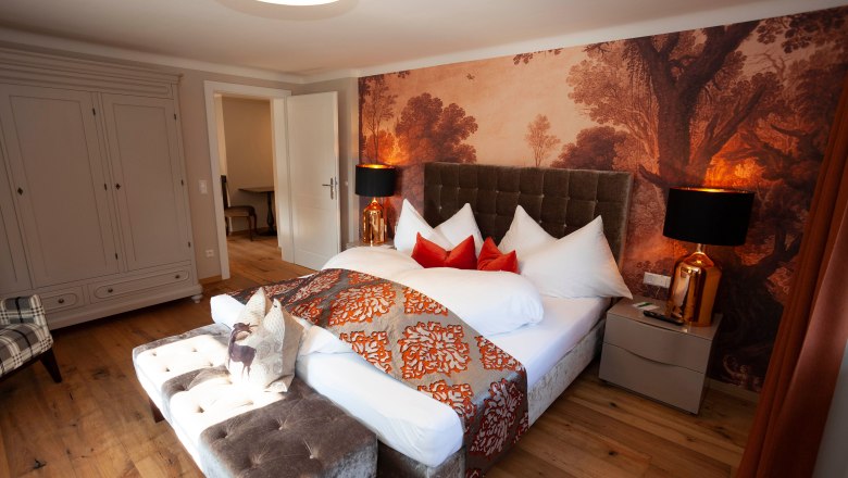 Elegant suite with large bed, decorative cushions and stylish wallpaper in Luberegg Castle.