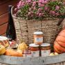 An arrangement of homemade specialties with pumpkin, jam, cake and flowers in a basket on a barrel.