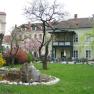 A garden with a pond and trees in front of a historic building with a balcony.
