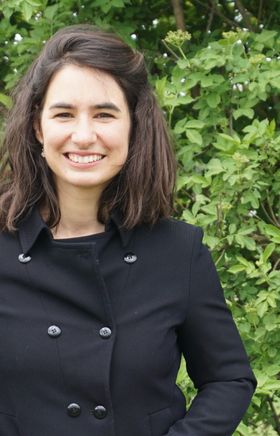 Eine Braunhaarige Frau lächelt, sie hat halblange Haare und trägt einen Mantel.