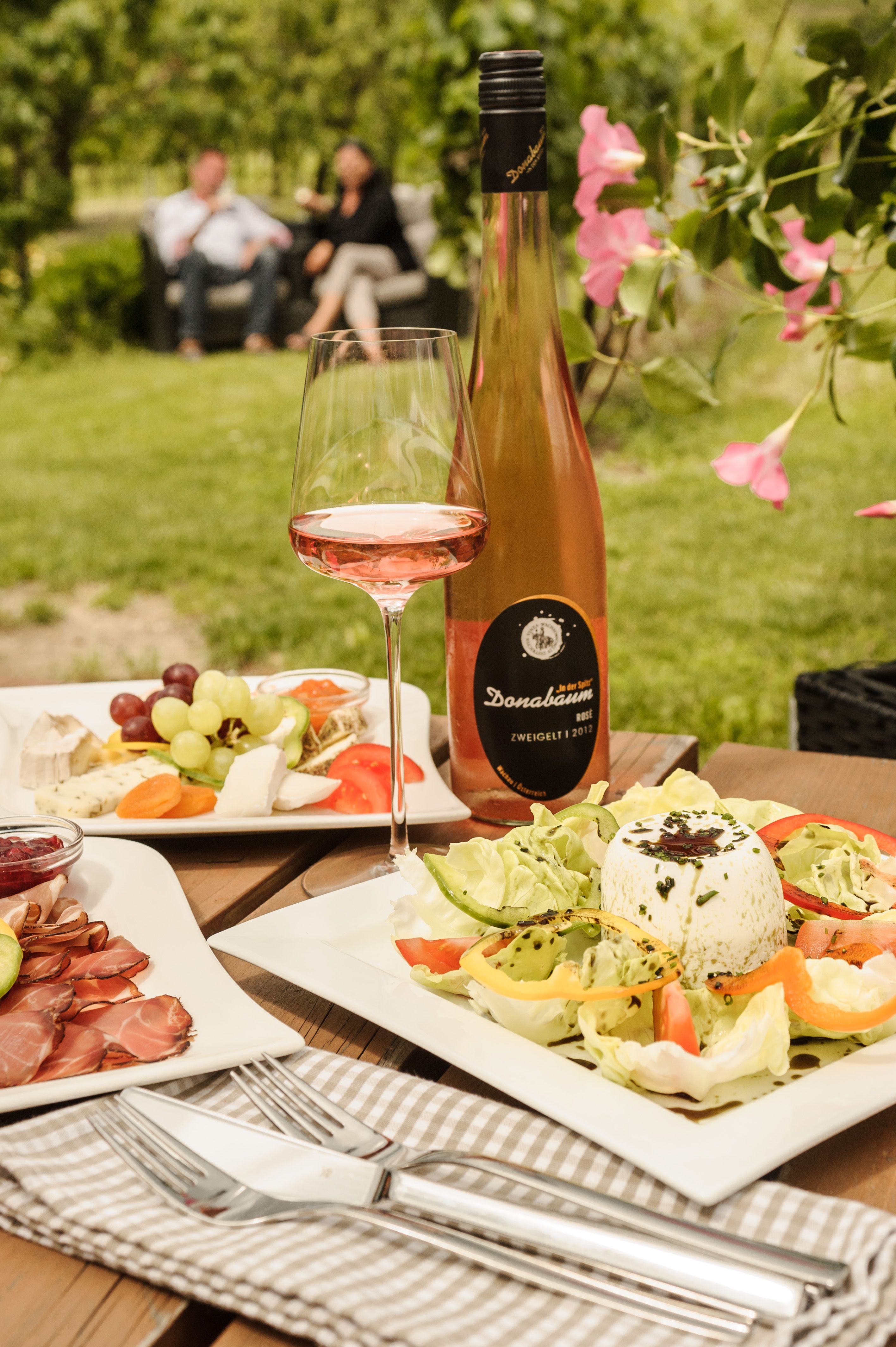 Ein gedeckter Tisch im Freien mit Wein, Salat und Käseplatte beim Heurigen Strawanzer