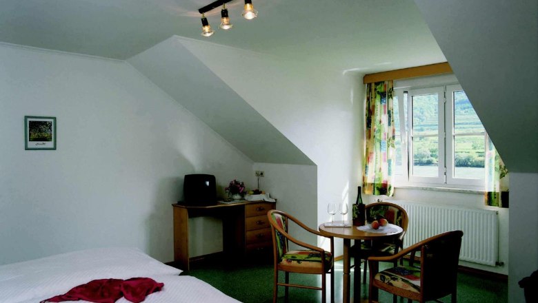 Gemütliches Zimmer mit Doppelbett, Tisch und Stühlen, Fenster mit Blick auf grüne Landschaft.