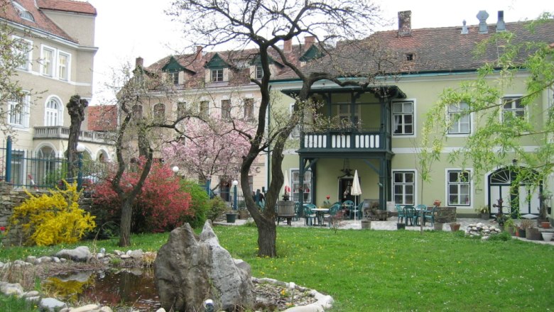 A garden with a pond and trees in front of a historic building with a balcony.