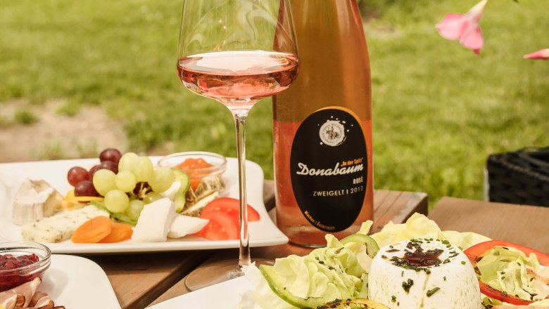 Ein gedeckter Tisch im Freien mit Wein, Salat und Käseplatte beim Heurigen Strawanzer