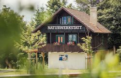 Ein idyllisches Haus neben einem Wald mit der Aufschrift Naturwerkstatt.