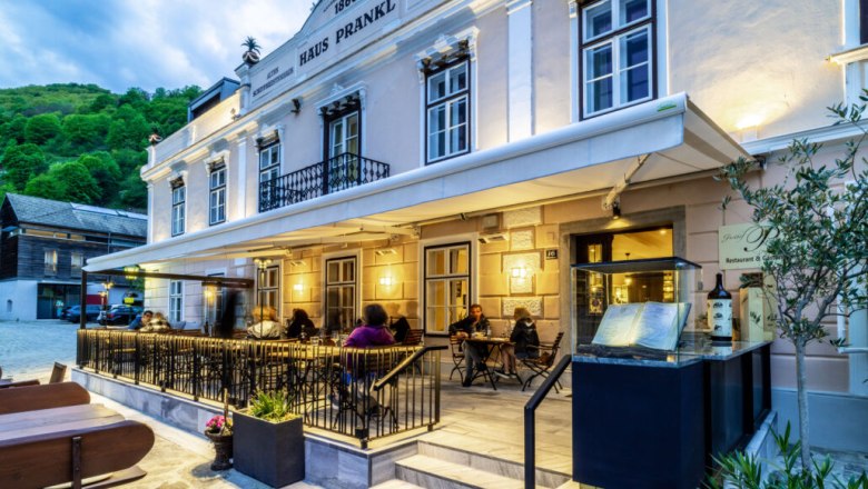 Exterior view of Gasthof Prankl with illuminated terrace and guests at tables.