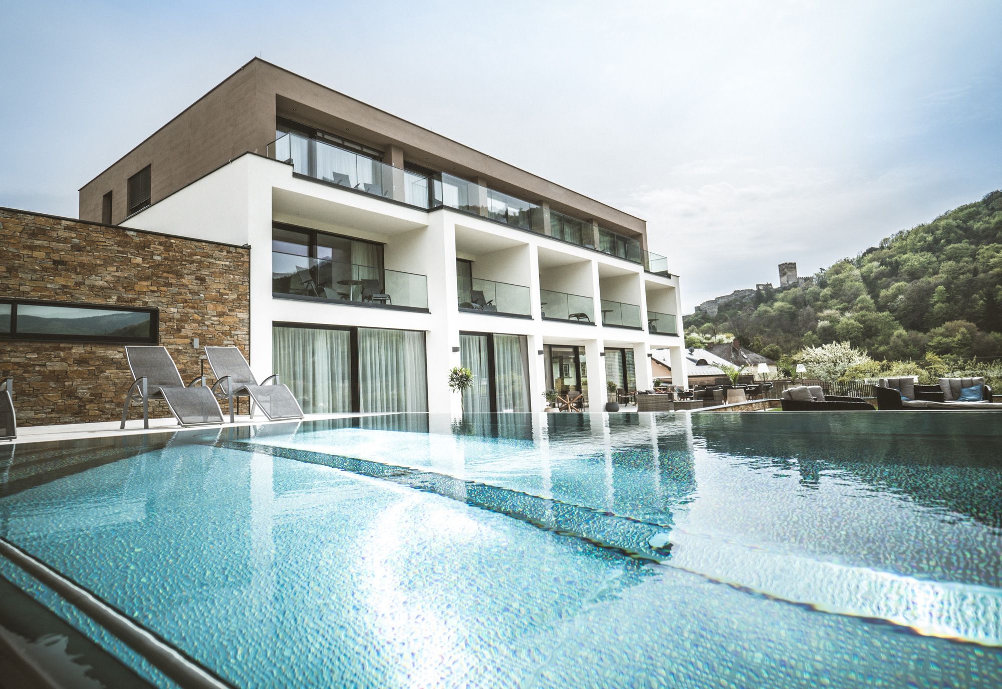 Modernes Boutiquehotel mit Pool und Liegestühlen, umgeben von grüner Landschaft.