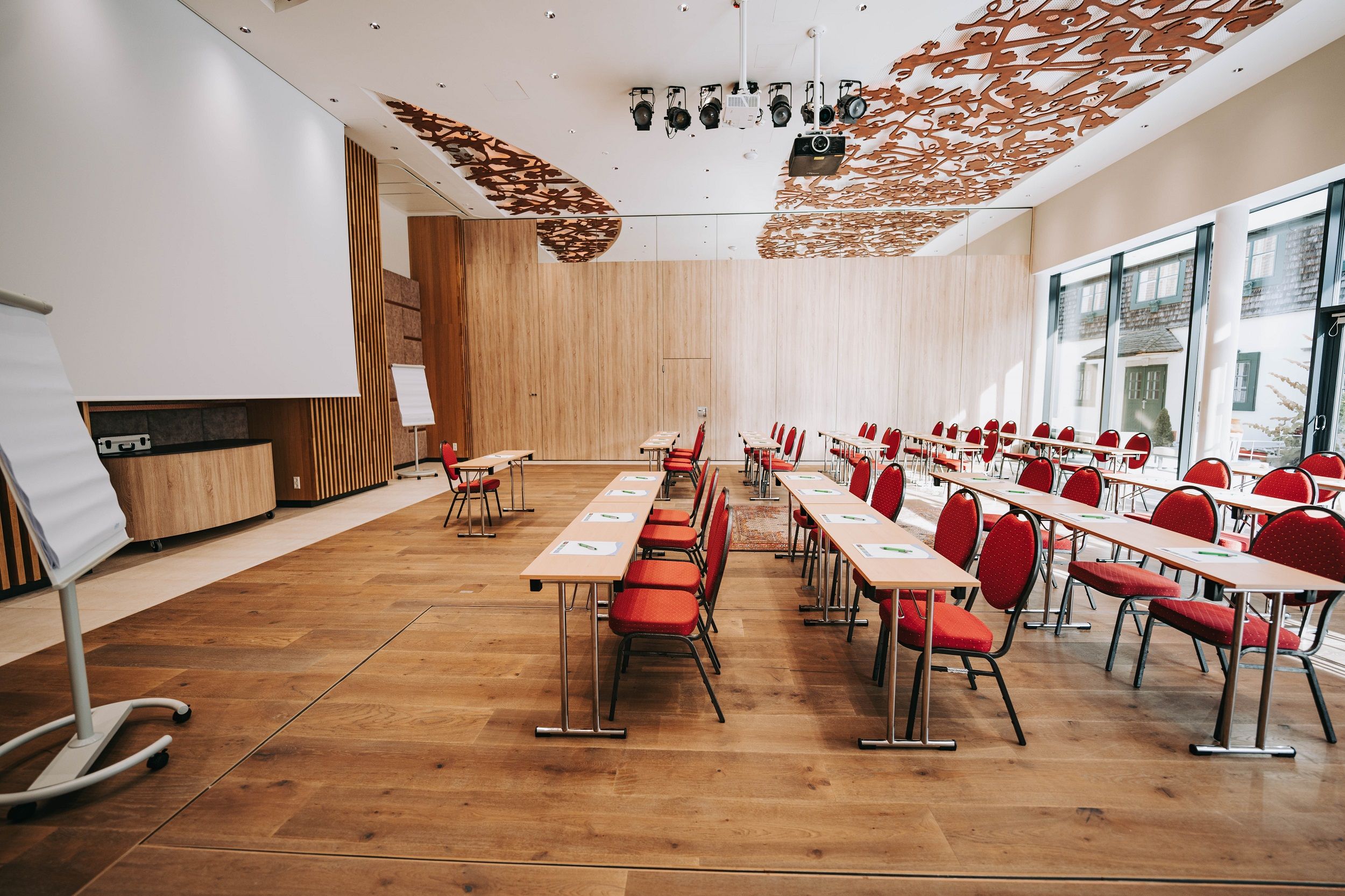 Innenansicht eines modernen Konferenzraums mit roten Stühlen und Holzboden.