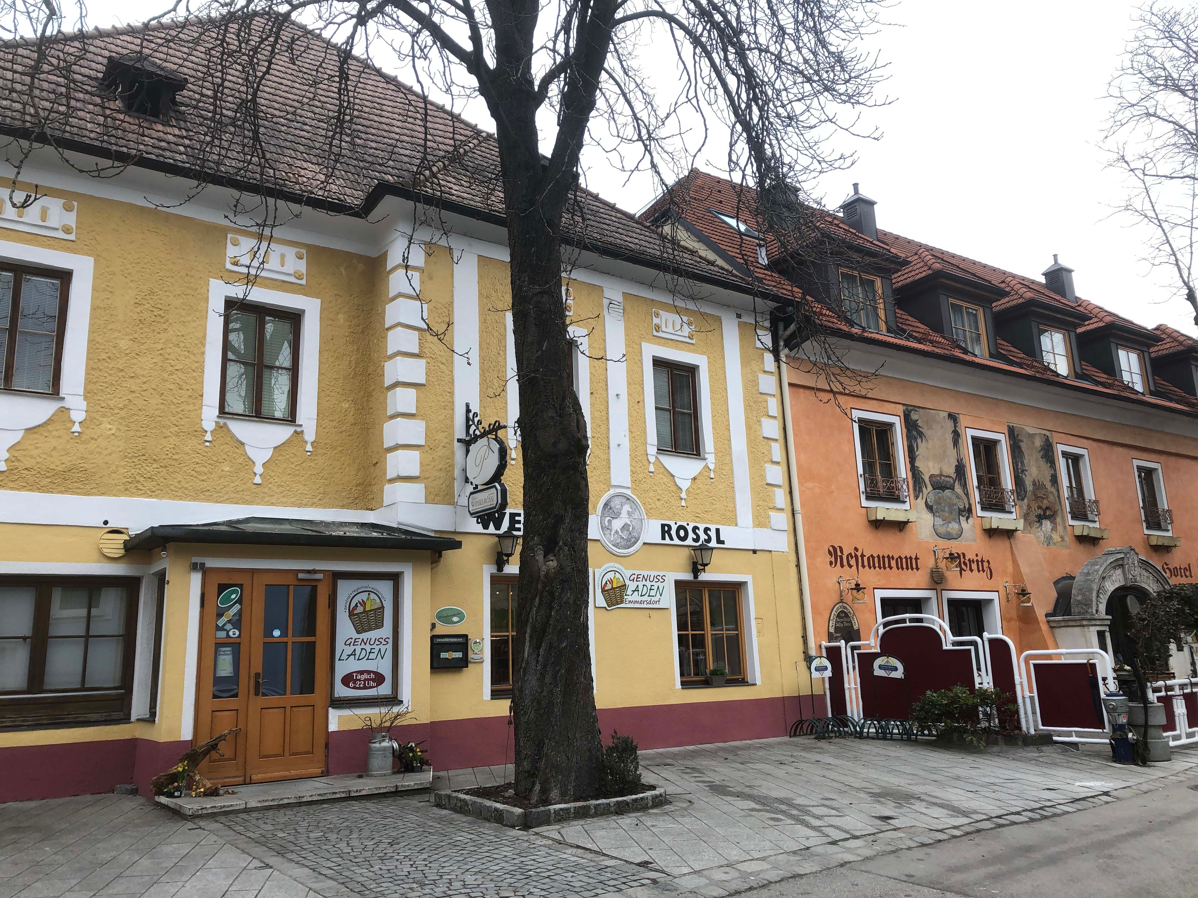 Außenansicht eines gelben Gebäudes mit Restaurant und Hotel, Baum im Vordergrund.