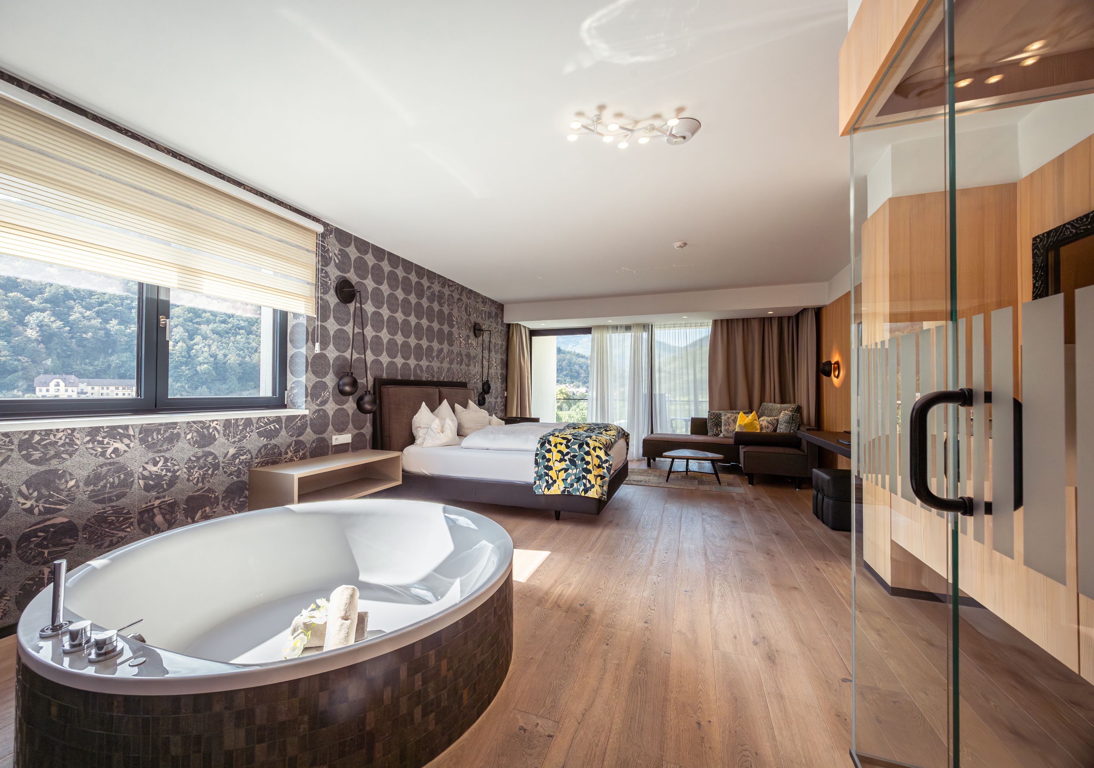Luxuriöses Hotelzimmer mit freistehender Badewanne, großem Bett und Panoramafenster mit Blick auf die Natur.