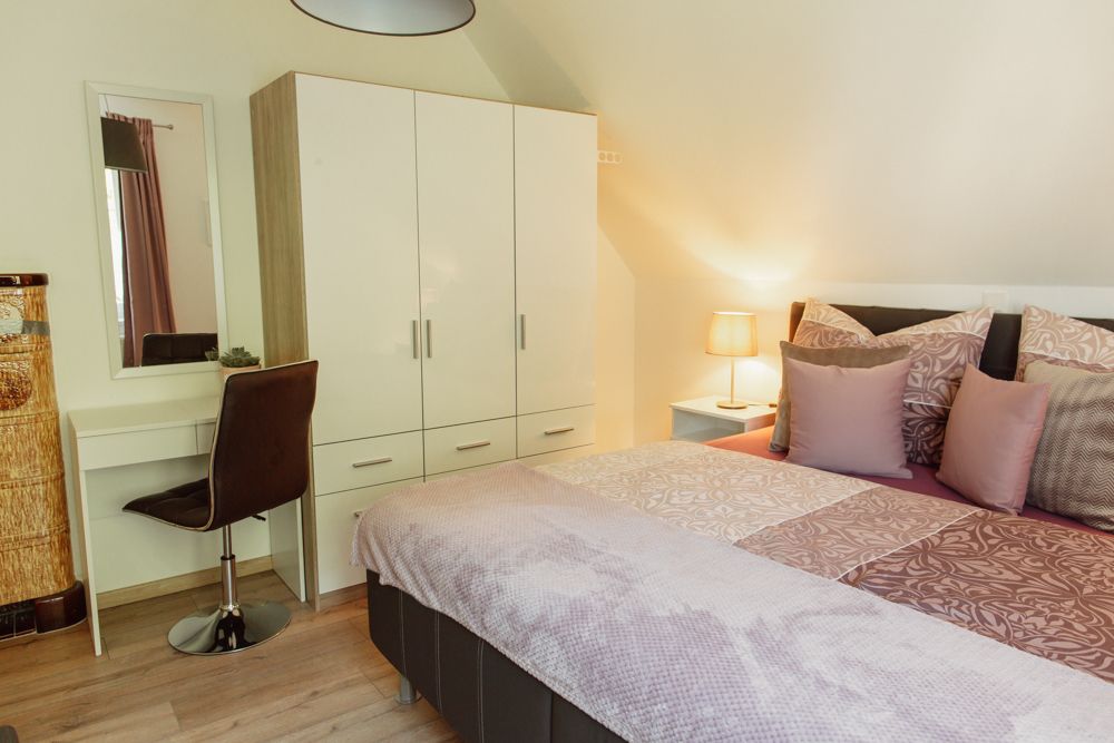 Schlafzimmer mit Doppelbett, Kleiderschrank, Schminktisch und Lampe.