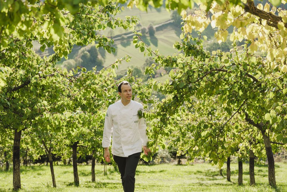 Roman Siebenhadl in weißer Kleidung geht durch einen Obstgarten mit grünen Bäumen.