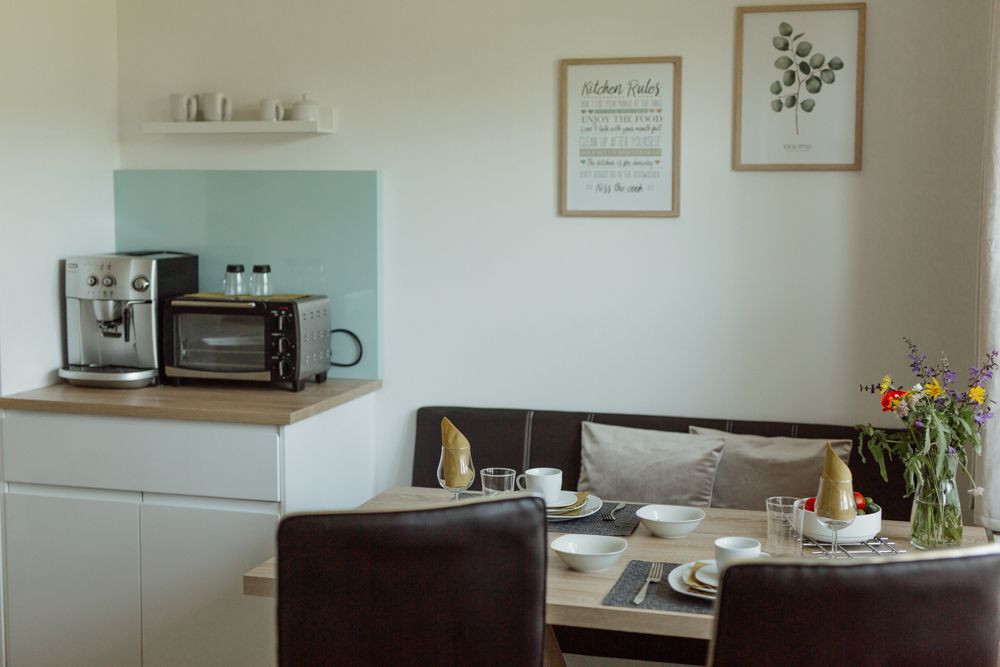 Kleine Küche mit Kaffeemaschine, Ofen, Esstisch und Blumen.