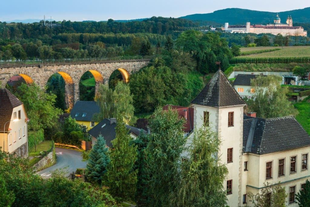 Eine Eisenbahnbrücke und ein kleines schloss, im Hintergrund das Stift Melk