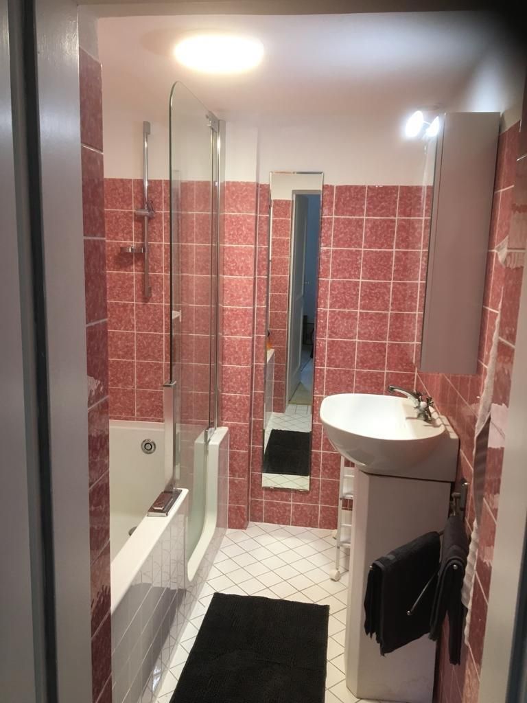 Kleines Badezimmer mit rosa Fliesen, Badewanne, Waschbecken und Spiegel.