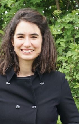 Eine Braunhaarige Frau lächelt, sie hat halblange Haare und trägt einen Mantel.